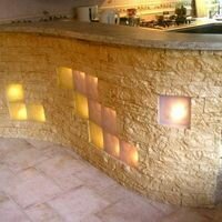 изогнутая барная стойка на кухне со стеклоблоками облагорожена искусственным камнем скалистый