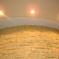 Круглая колонна в холле частного дома отделана интерьерным камнем скалистый молочного цвета