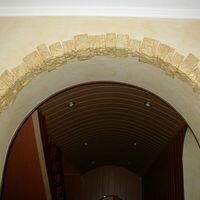 наружные углы полукруглой арки в гостиной частного дома украшены диким камнем скалистый песочного цвета