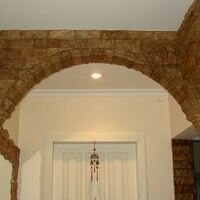 полукруглая арка и ригель в прихожей квартиры отделаны интерьерным камнем скалистый темного чайного цвета