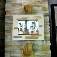 стена из дикого камня греческий сланец в интерьере магазина украшена креативным декором в виде рук, которые держат телевизор